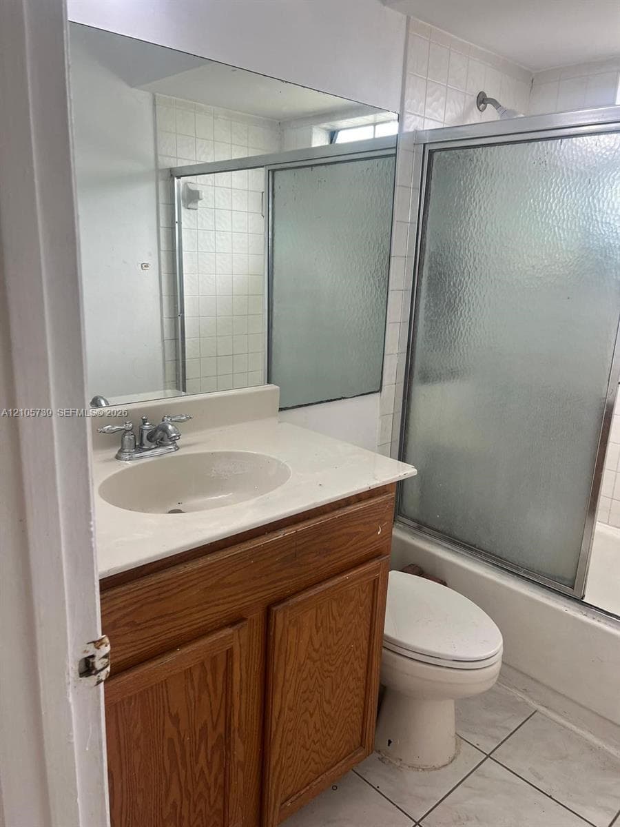 Vanity featuring a light-toned countertop with an integrated oval basin and wood-finish cabinetry, complemented by a large wall-mounted mirror, ceramic tile flooring, and a shower-tub combination with a sliding glass enclosure