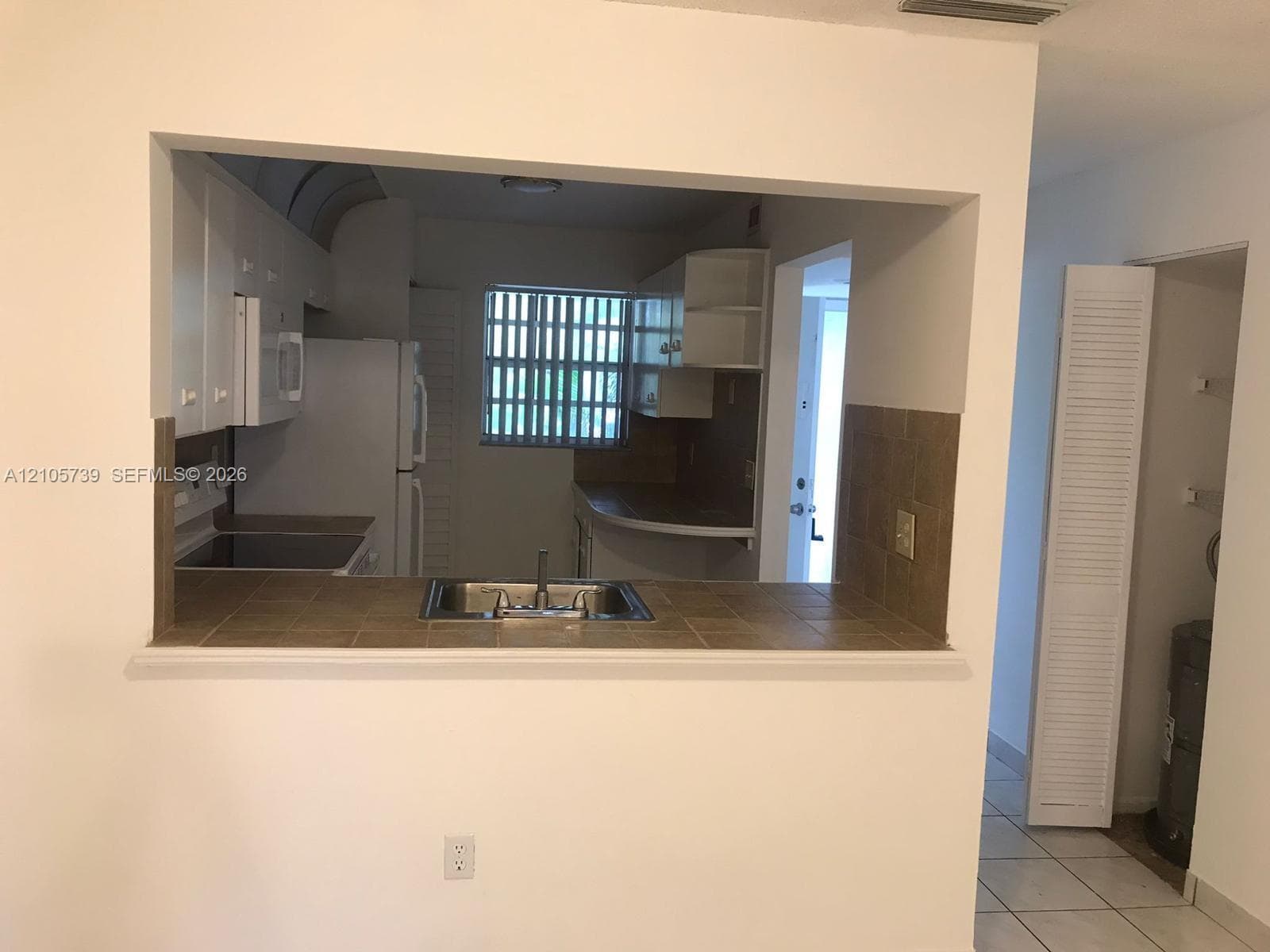 Kitchen featuring a tiled pass-through breakfast bar, stainless steel drop-in sink, white cabinetry, ceramic tile countertops, and louvered closet doors
