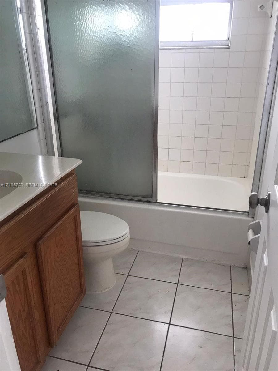 Bathroom featuring a wood-finish vanity, solid-surface countertop, sliding glass shower door, and tile flooring