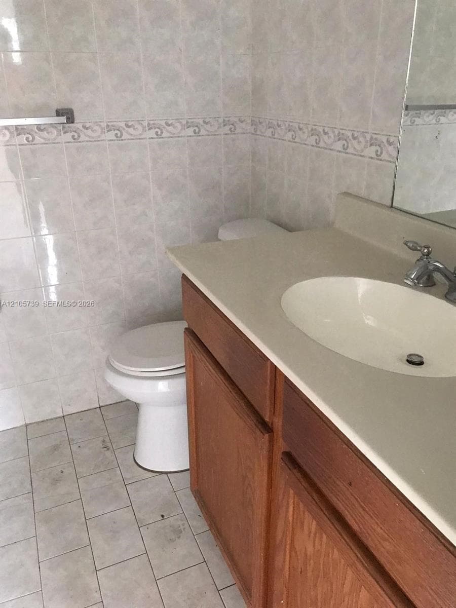 Bathroom featuring a wood-finish vanity with a neutral solid-surface countertop, integrated basin, wall-mounted mirror, and floor-to-ceiling ceramic tile wall detailing