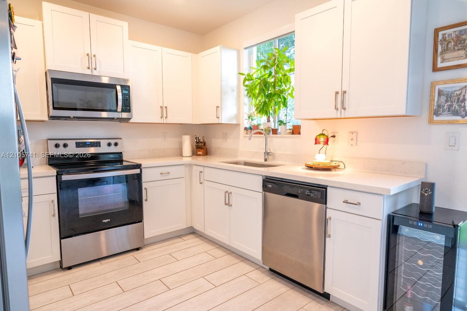 Kitchen featuring white shaker-style cabinetry, stainless steel appliances, light-toned solid surface countertops, a stainless steel undermount sink, and wood-finish tile flooring