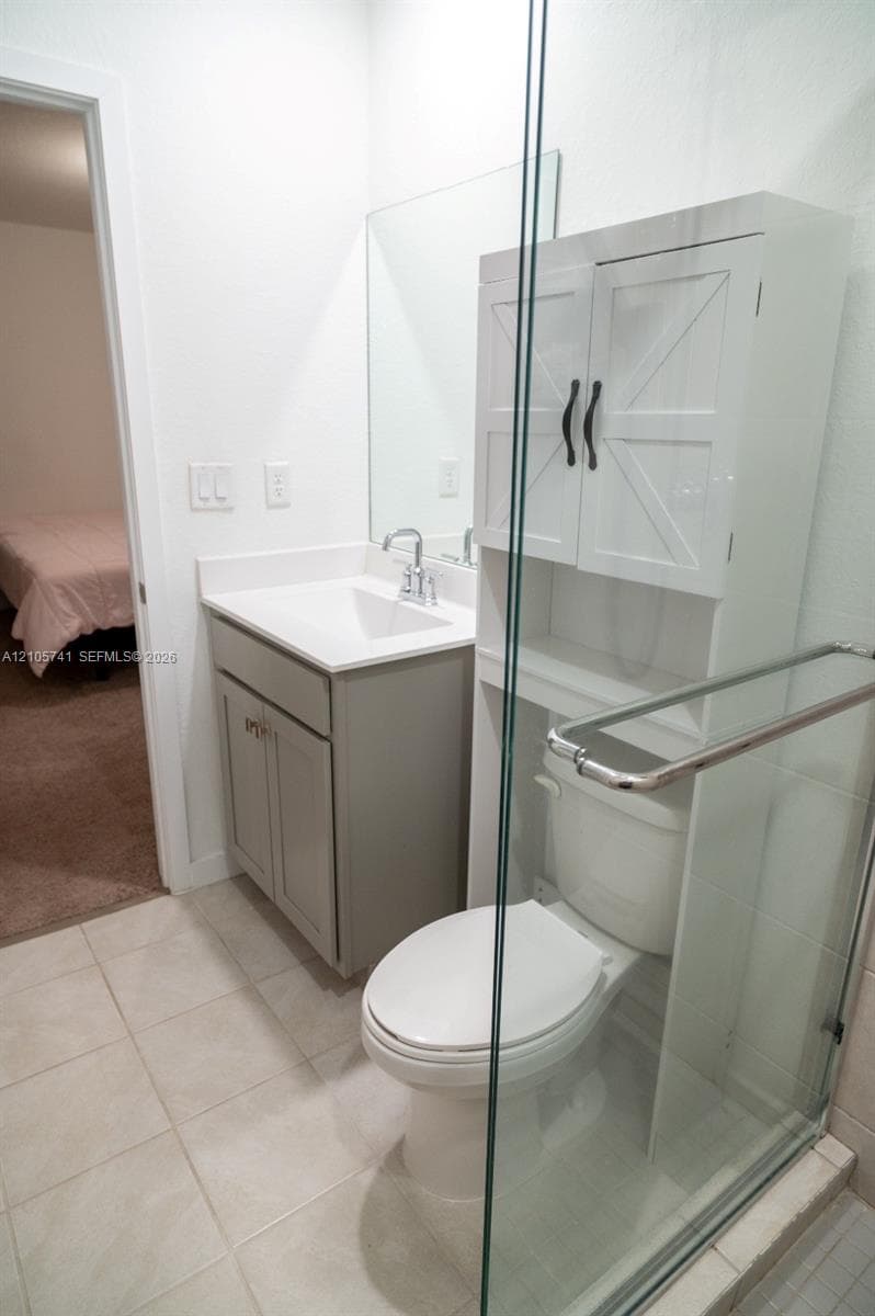 Bathroom featuring a vanity with a white countertop and integrated sink, a frameless glass shower enclosure, a white over-the-toilet storage cabinet, and large-format tile flooring
