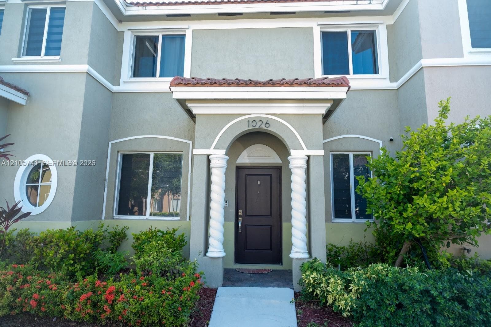 Stucco exterior featuring an arched entryway with decorative spiral columns, a portico with tile roofing, and a circular accent window