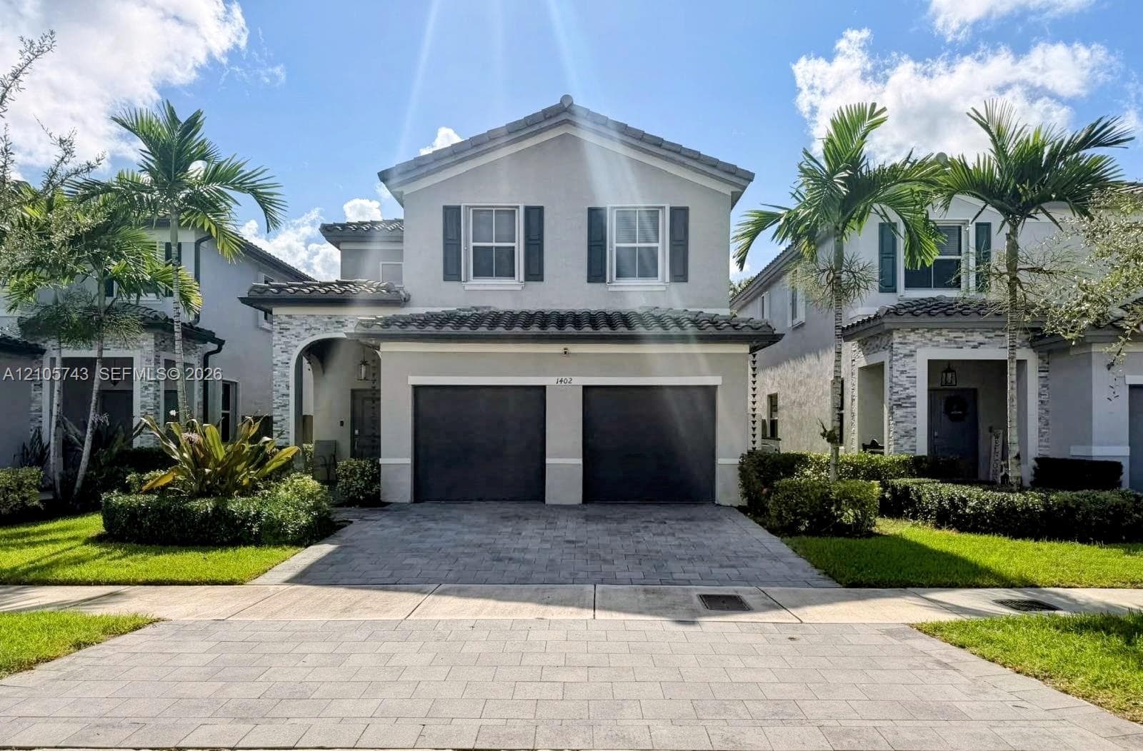 Two-story residence featuring a tile roof, paver driveway, stone-veneer accent siding, two-car garage, and shutter-framed windows