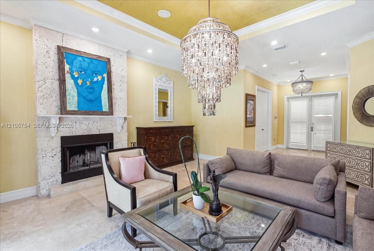 Fireplace with a coral stone facade, tiered crystal chandelier, coffered ceiling with gold-leaf accents, recessed lighting, and large-format tile flooring