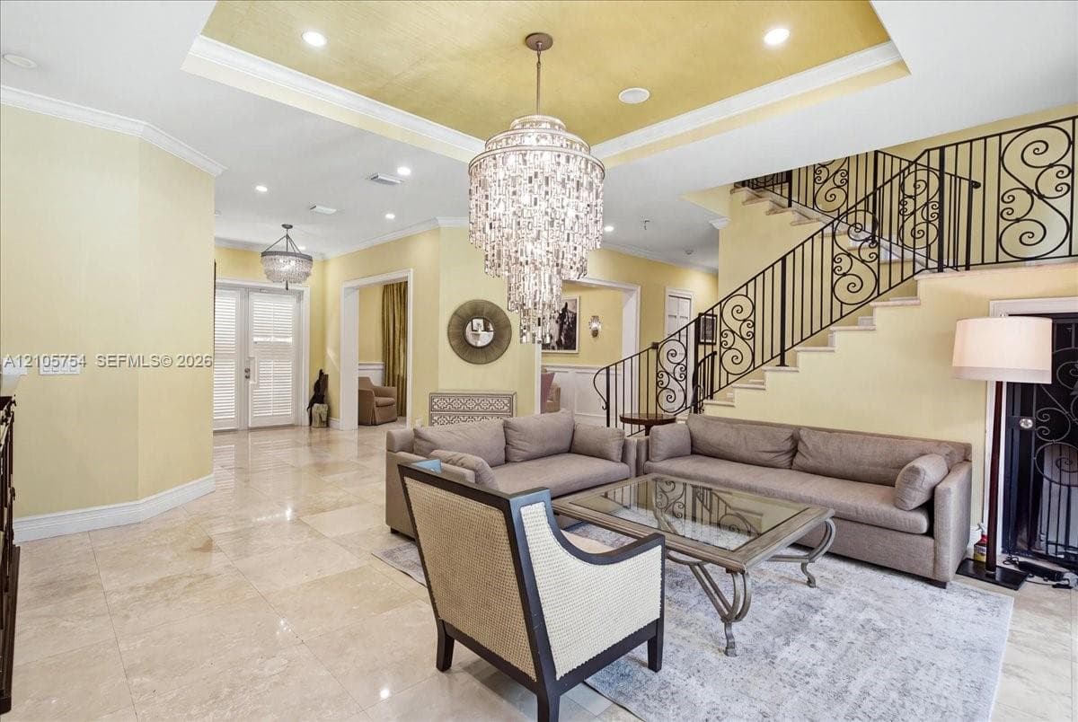 Foyer featuring large-format stone flooring, a tray ceiling with recessed lighting, a tiered crystal chandelier, and an open staircase with decorative wrought-iron railings