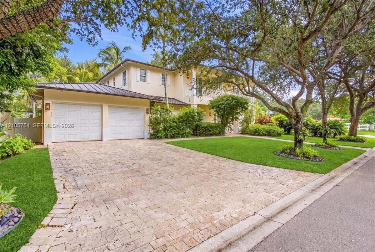 Two-story residence featuring a paved stone driveway, two-car garage, metal roof, and manicured landscaping