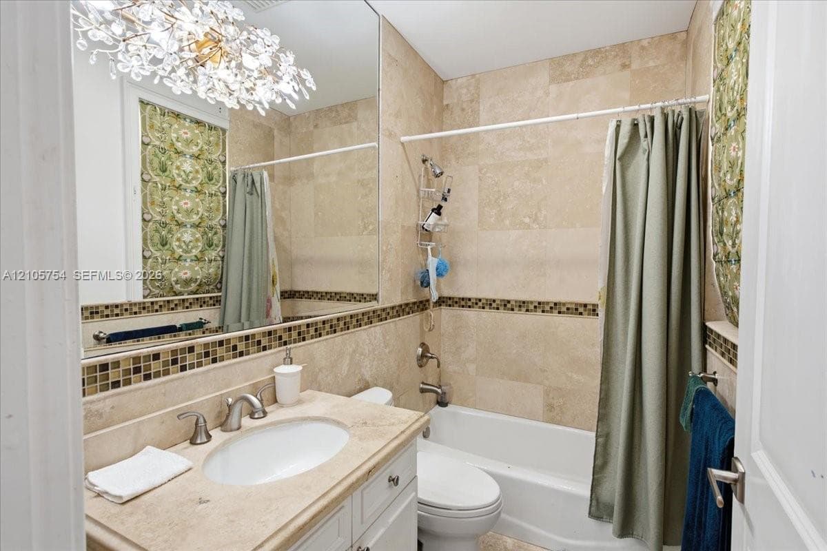Full-height wall-mounted mirror, natural stone tile shower surround, mosaic tile inlay, crystal-style chandelier, and undermount sink with stone vanity top