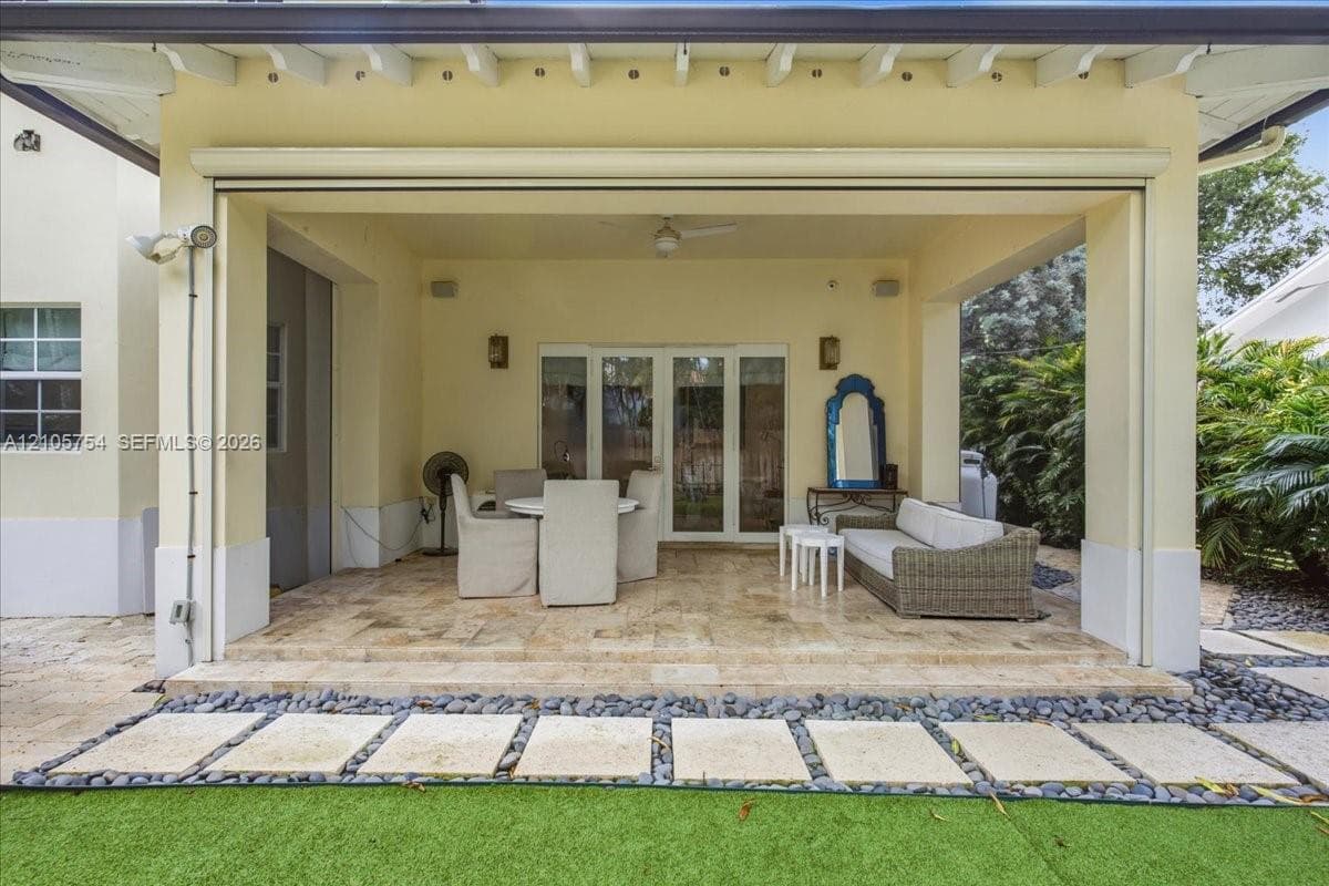 Covered patio featuring stone-tile flooring, integrated ceiling fan, recessed wall sconces, and multi-panel glass door entry, accented by a stone paver walkway