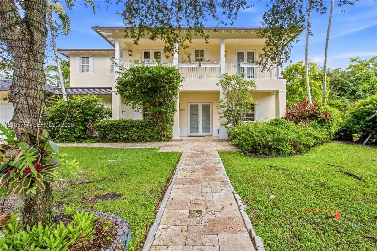 Two-story residence featuring a covered second-story balcony with white railing, stone-paver walkway, and symmetrical exterior columns