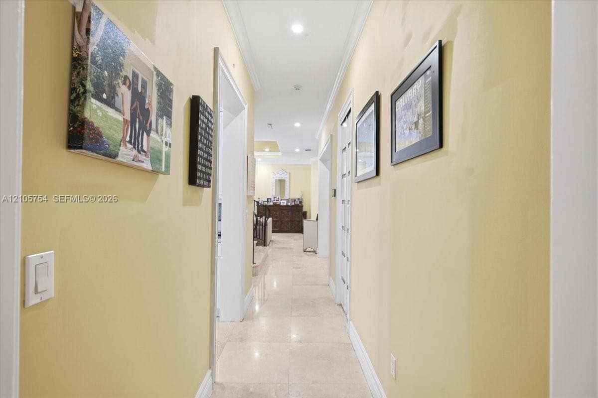Hallway featuring light-toned stone tile flooring, recessed ceiling lighting, and crown molding