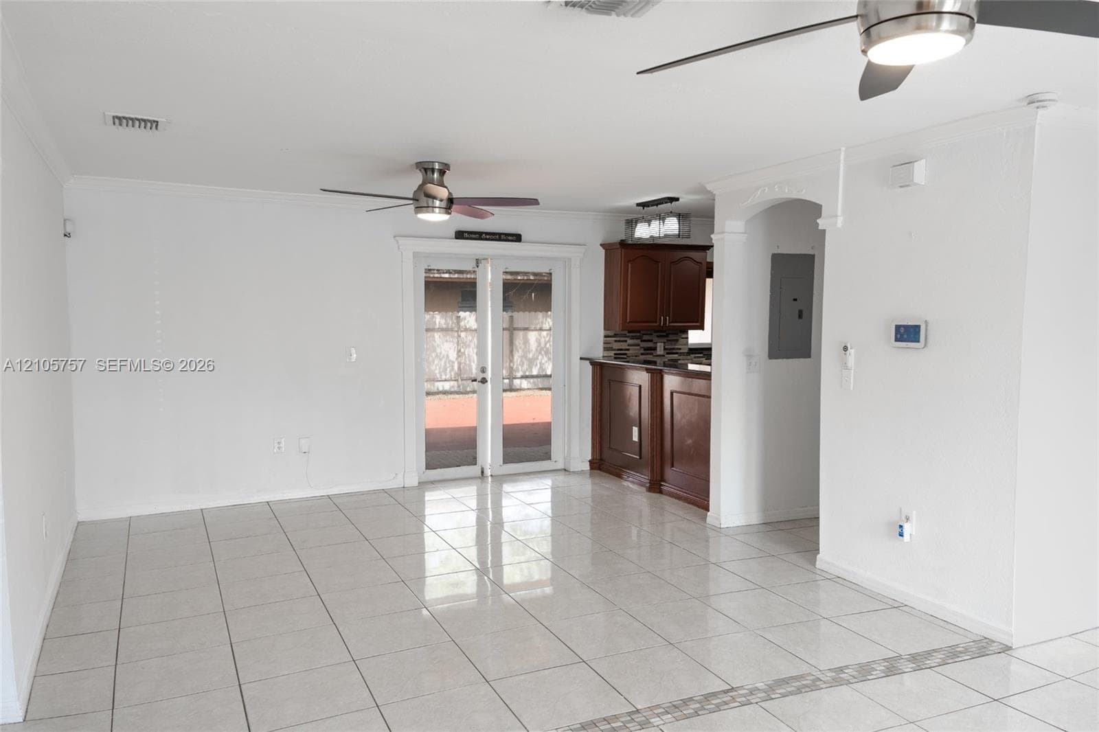 Open living space featuring tile flooring, dual ceiling fans, French doors, and a kitchen peninsula with dark-finish cabinetry