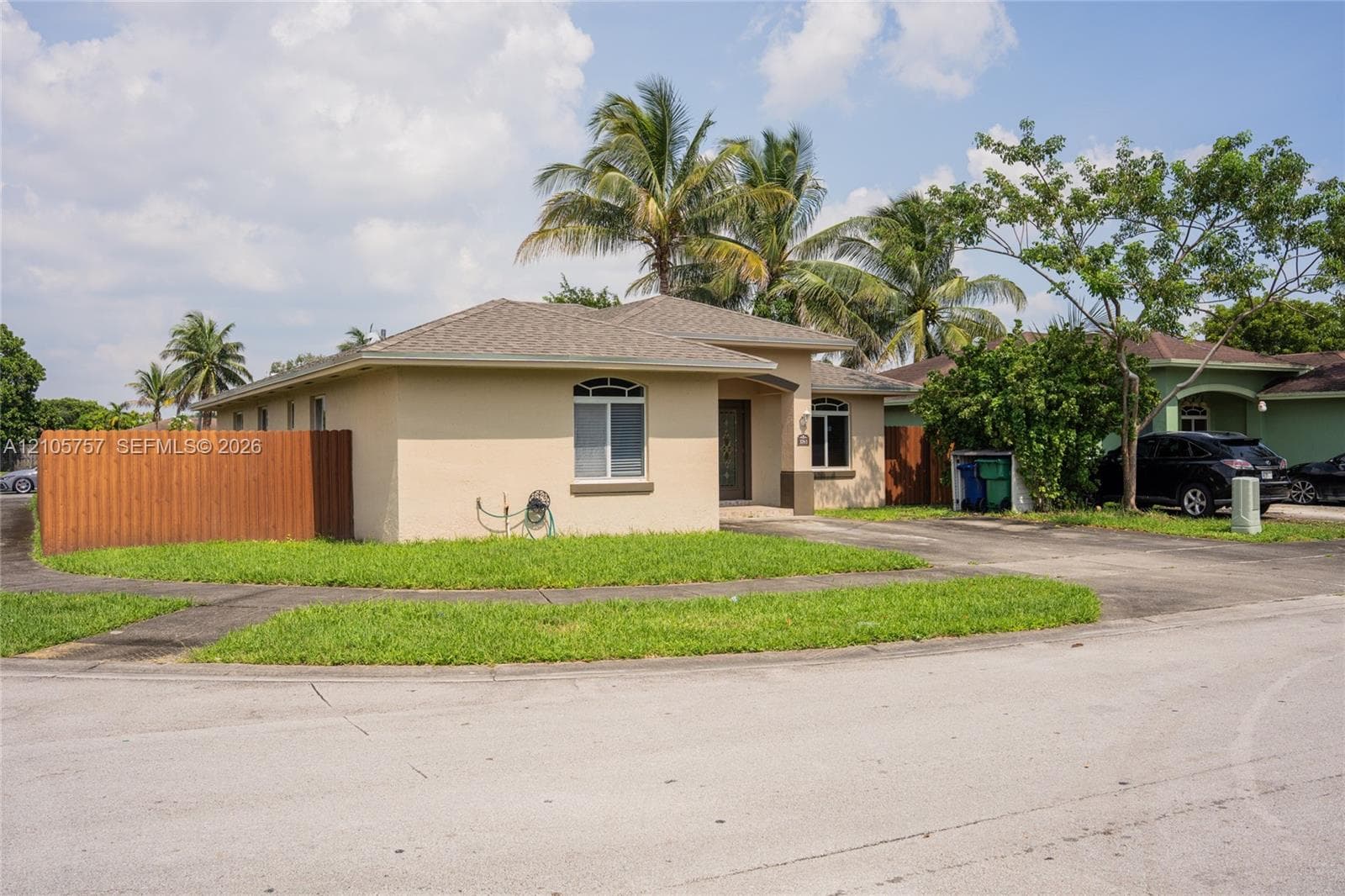 Single-story residence featuring a hipped roofline, stucco exterior, arched window detailing, and a wood-slat perimeter fence