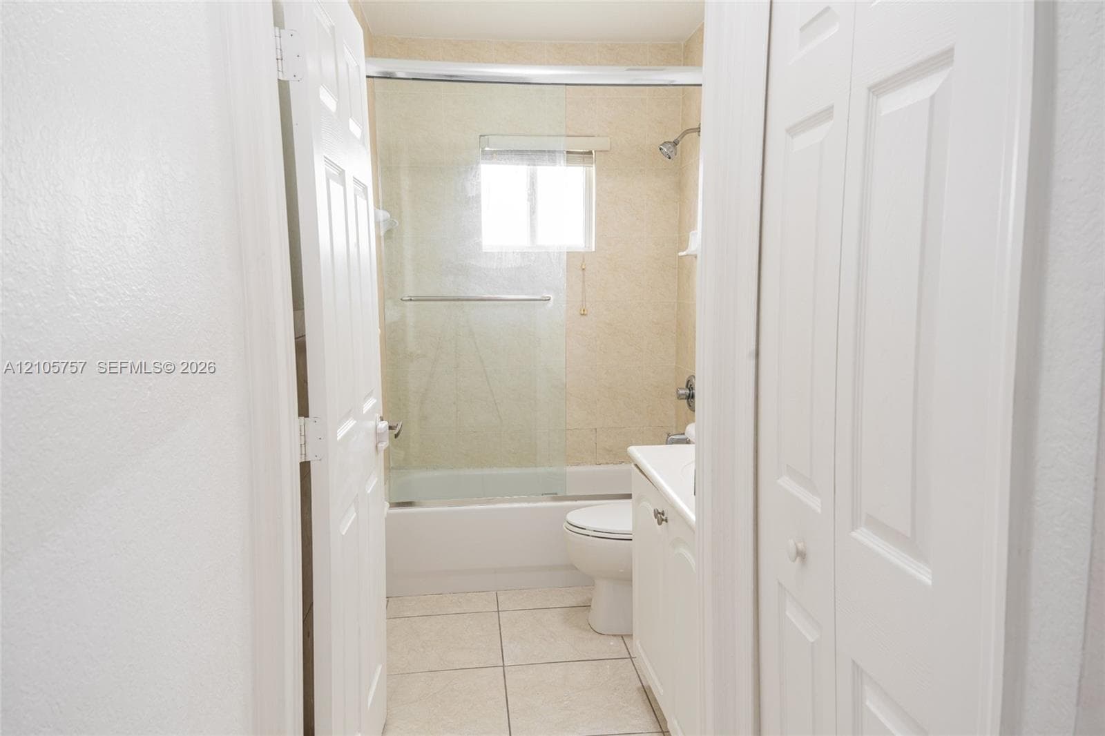 Bathroom featuring a glass-enclosed shower and tub combination, light-toned ceramic tile flooring, and a white vanity cabinet