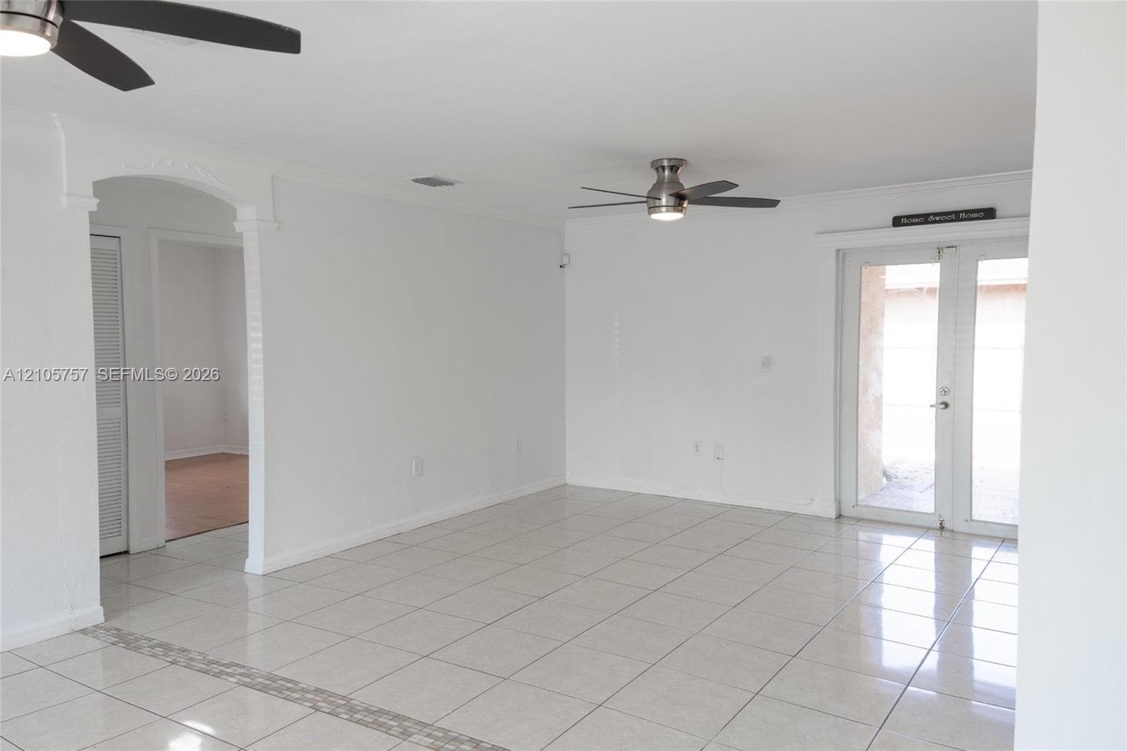 Interior space featuring large-format neutral tile flooring, arched doorways, dual ceiling fans with integrated lighting, and glass-paneled double doors