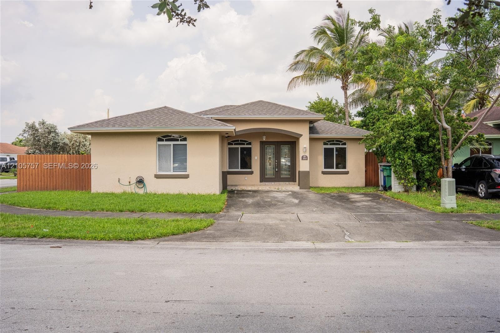 Single-story exterior featuring a stucco facade, hipped roof, dual-entry glass panel doors, arched window accents, and a concrete driveway