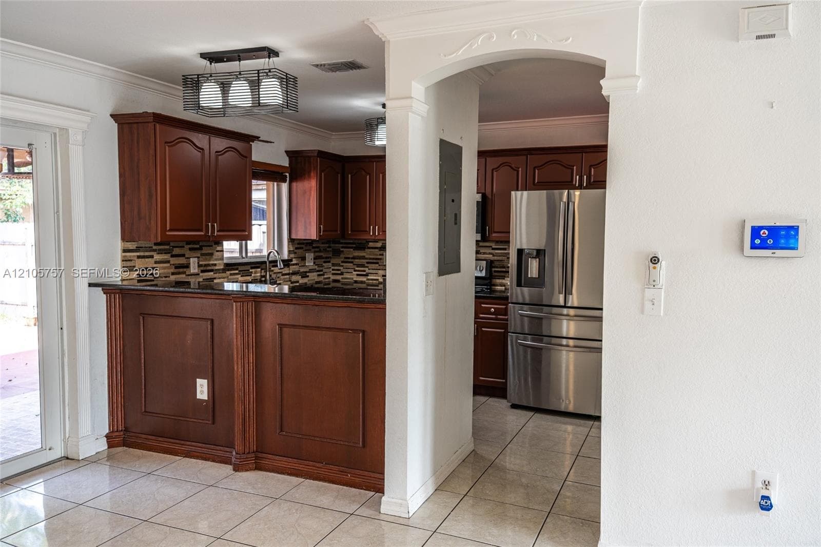 Kitchen featuring dark wood cabinetry, a breakfast bar, stone-tile backsplash, stainless steel refrigerator, and tiled flooring