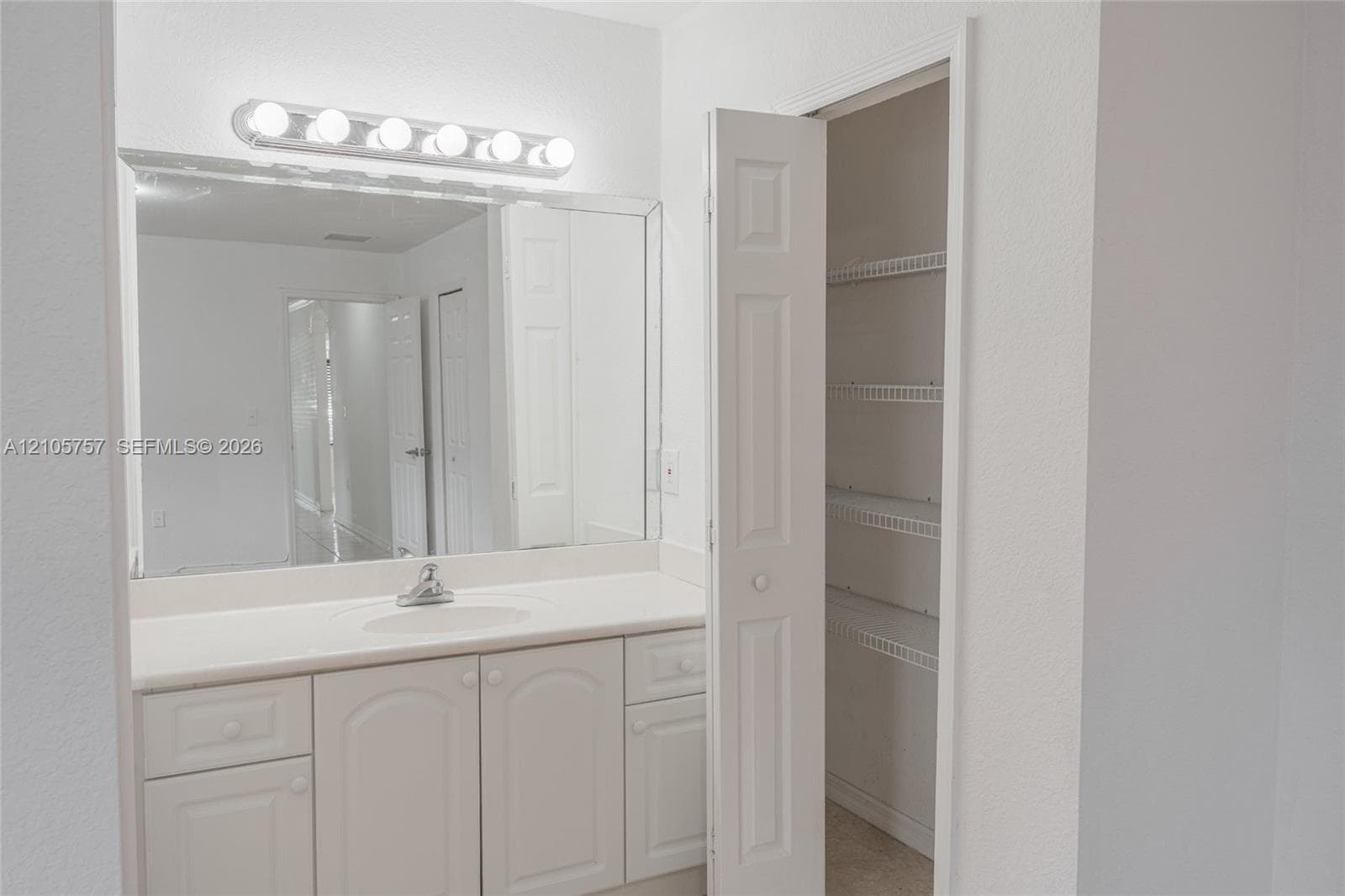 Vanity featuring an integrated sink, solid-surface countertop, multi-drawer cabinetry, wall-to-wall mirror, and multi-bulb light fixture, complemented by an integrated closet with wire shelving