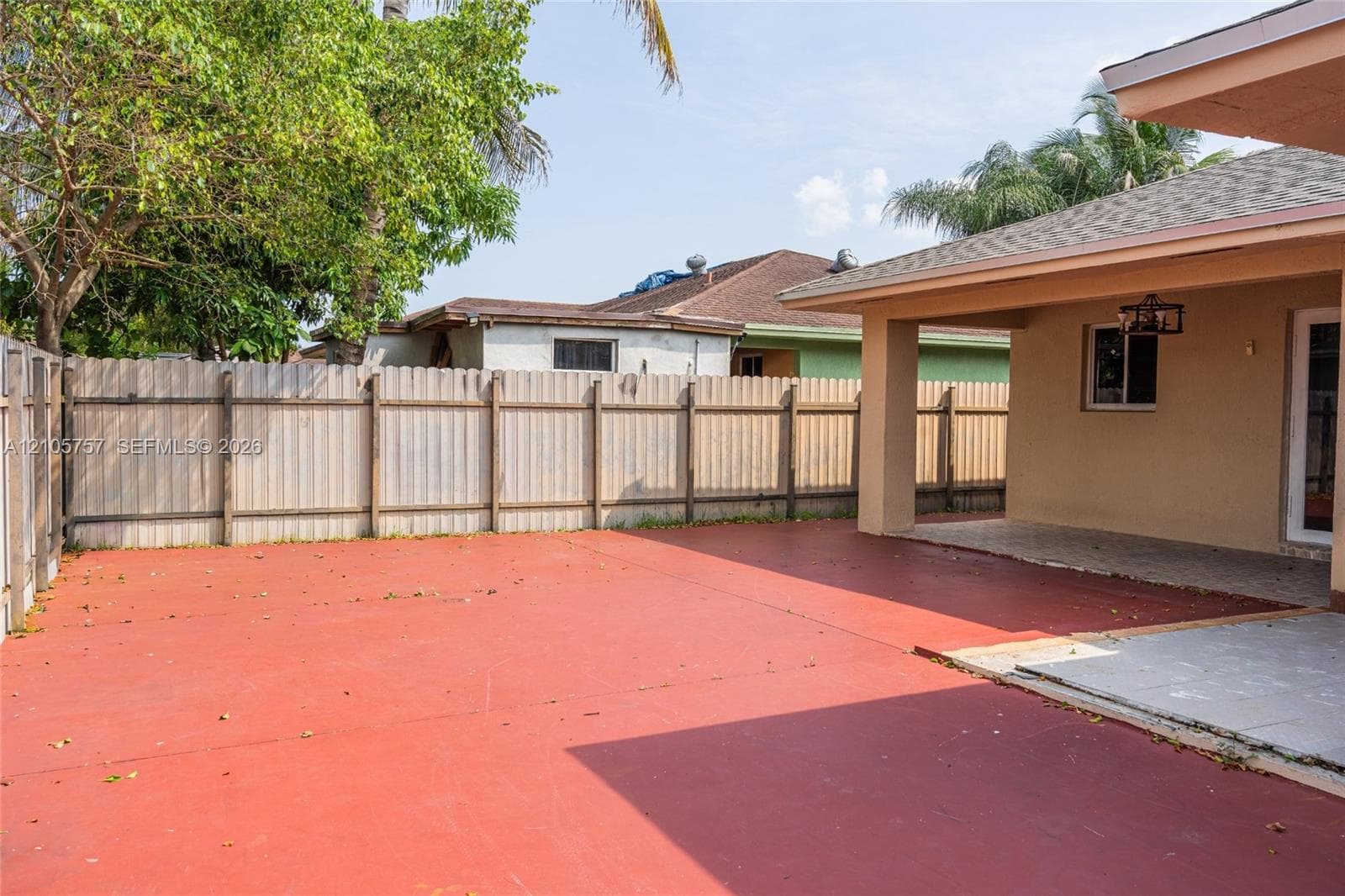 Rear exterior space featuring a covered patio, expansive concrete hardscaping, and full-height perimeter wood fencing