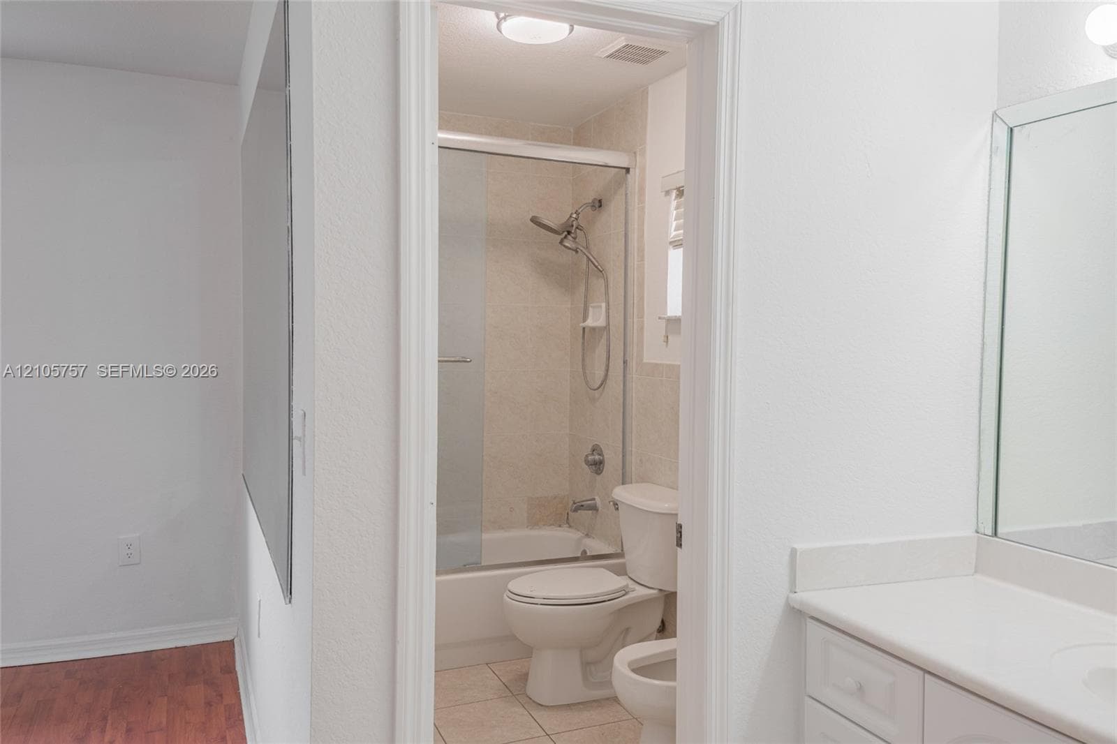 Bathroom featuring a white vanity cabinet, solid-surface countertop, rectangular wall mirror, tile flooring, and a tub-shower combination with sliding glass doors