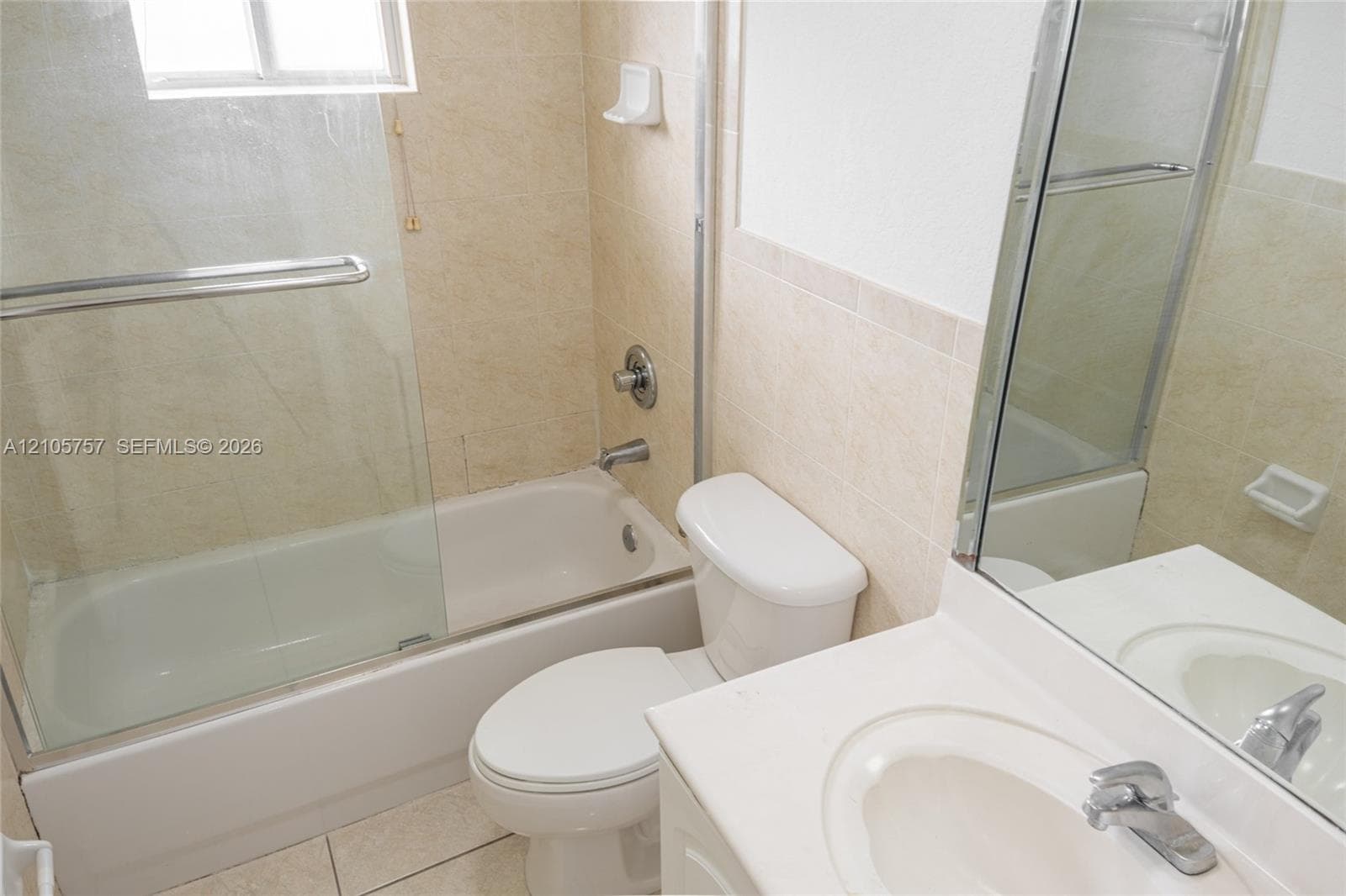 Full bathroom featuring a tub-shower combination with a glass door, light-toned wall tile, a vanity with a white countertop, and a built-in recessed medicine cabinet