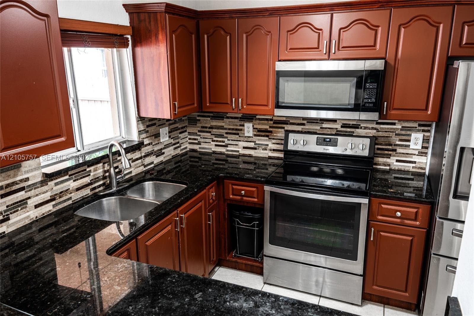 Kitchen featuring wood cabinetry, stone countertops, multi-toned tile backsplash, and stainless steel appliances including a built-in microwave and range