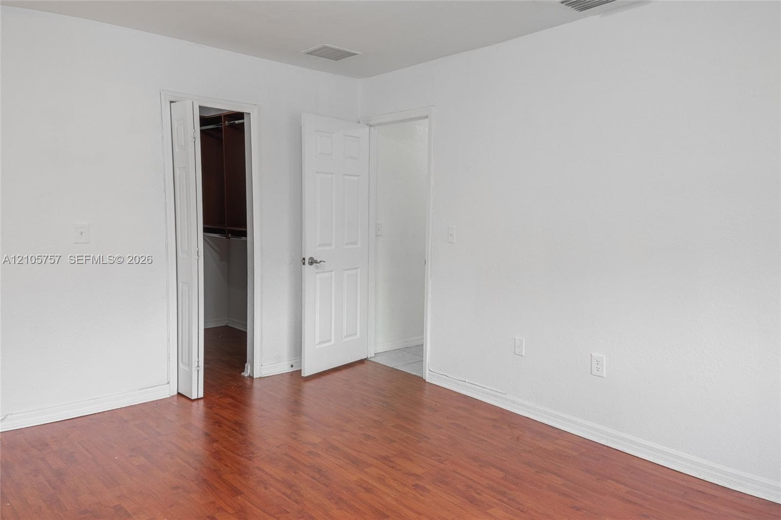 Room featuring wood-finish flooring, white walls, six-panel interior doors, and a reach-in closet with built-in shelving