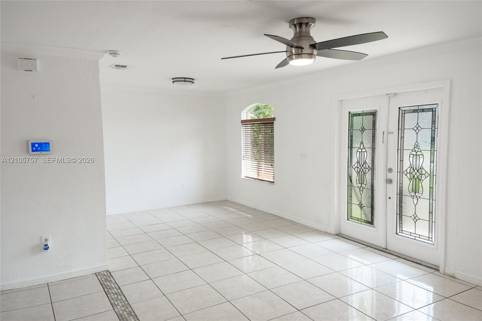Double entry doors with stained glass inserts, neutral tile flooring, brushed nickel ceiling fan with integrated lighting, and an arched window