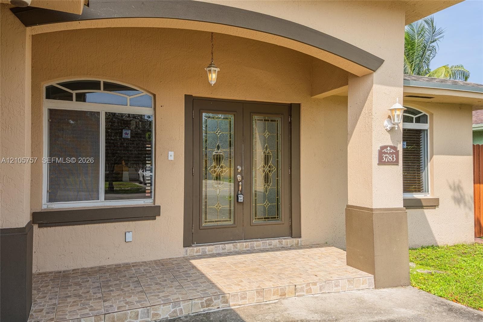 Covered entryway featuring an arched roofline, double glass-insert doors, tile flooring, and decorative exterior wall-mounted lighting