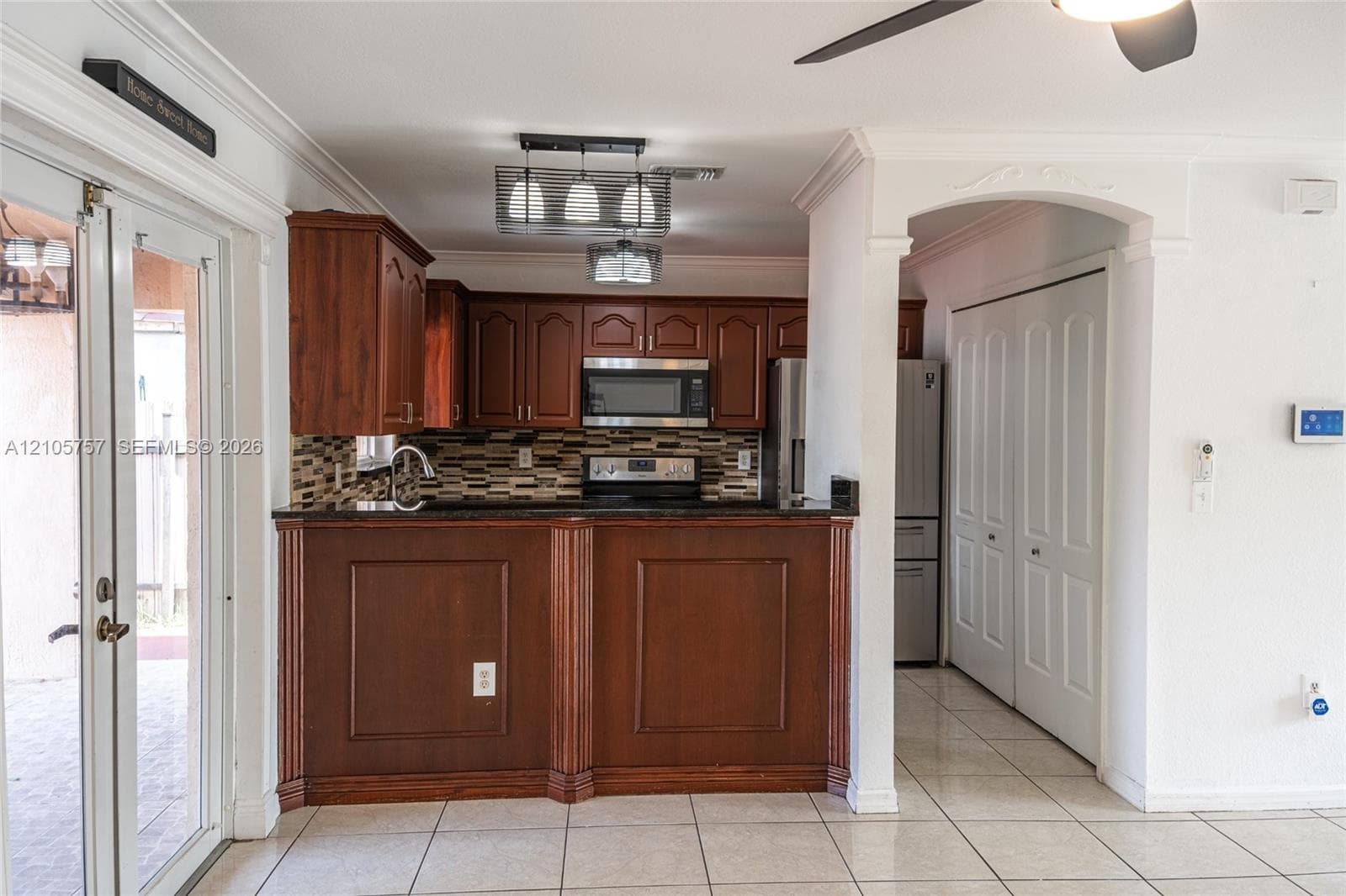 Kitchen featuring wood cabinetry, dark stone countertops, decorative tile backsplash, stainless steel appliances, and a peninsula with millwork detailing