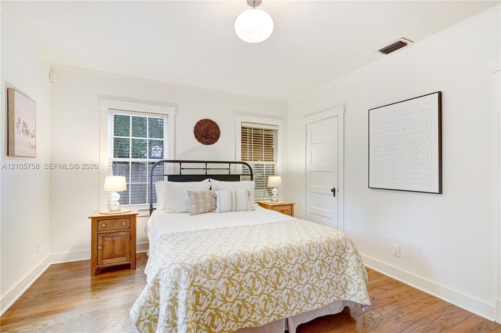 Room featuring wood-finish flooring, two double-hung windows with exterior grid muntins, a white-paneled interior door, and a spherical pendant light fixture