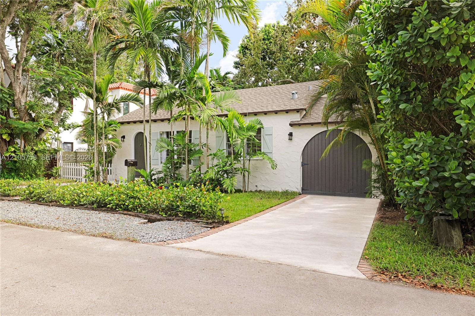 Single-story residence featuring a textured stucco exterior, arched front entryway, arched garage door, shuttered windows, and a concrete driveway