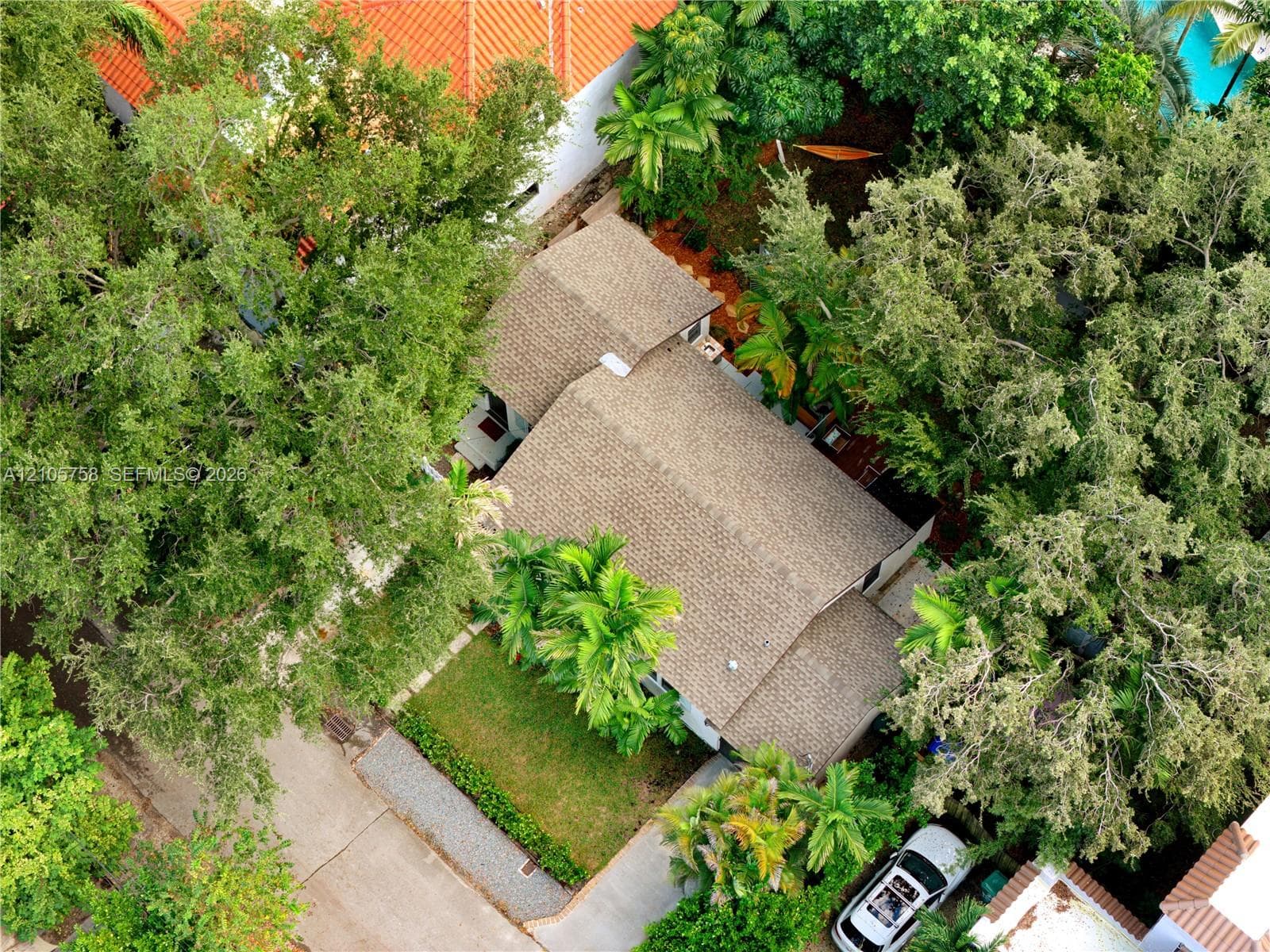 Aerial perspective featuring a multi-pitched roof with textured shingles, mature perimeter trees, manicured lawn, and stone-paver walkway
