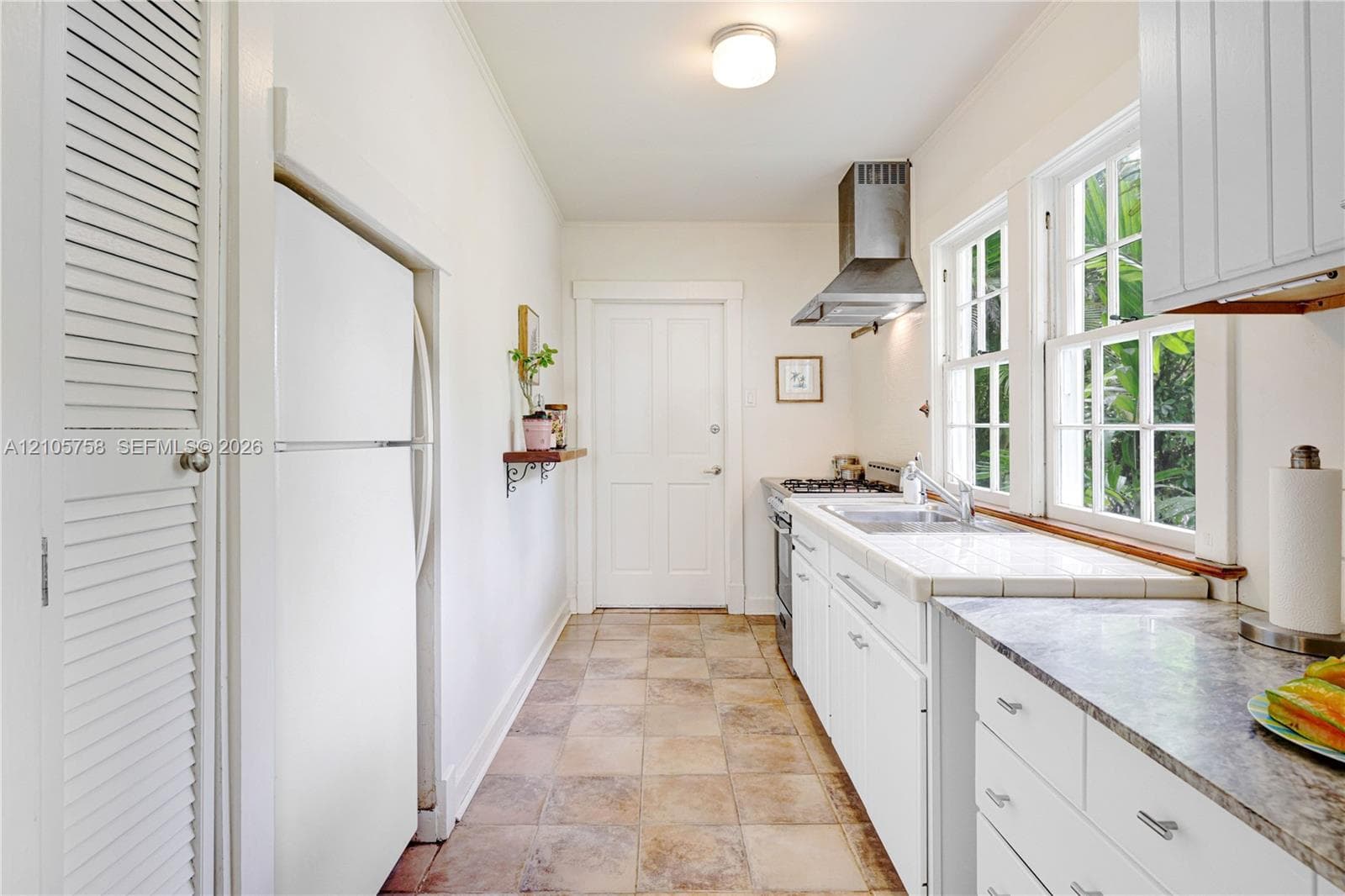 Kitchen featuring white shaker-style cabinetry, a stainless steel range hood, stone-finish countertops, tile flooring, and dual-sash windows