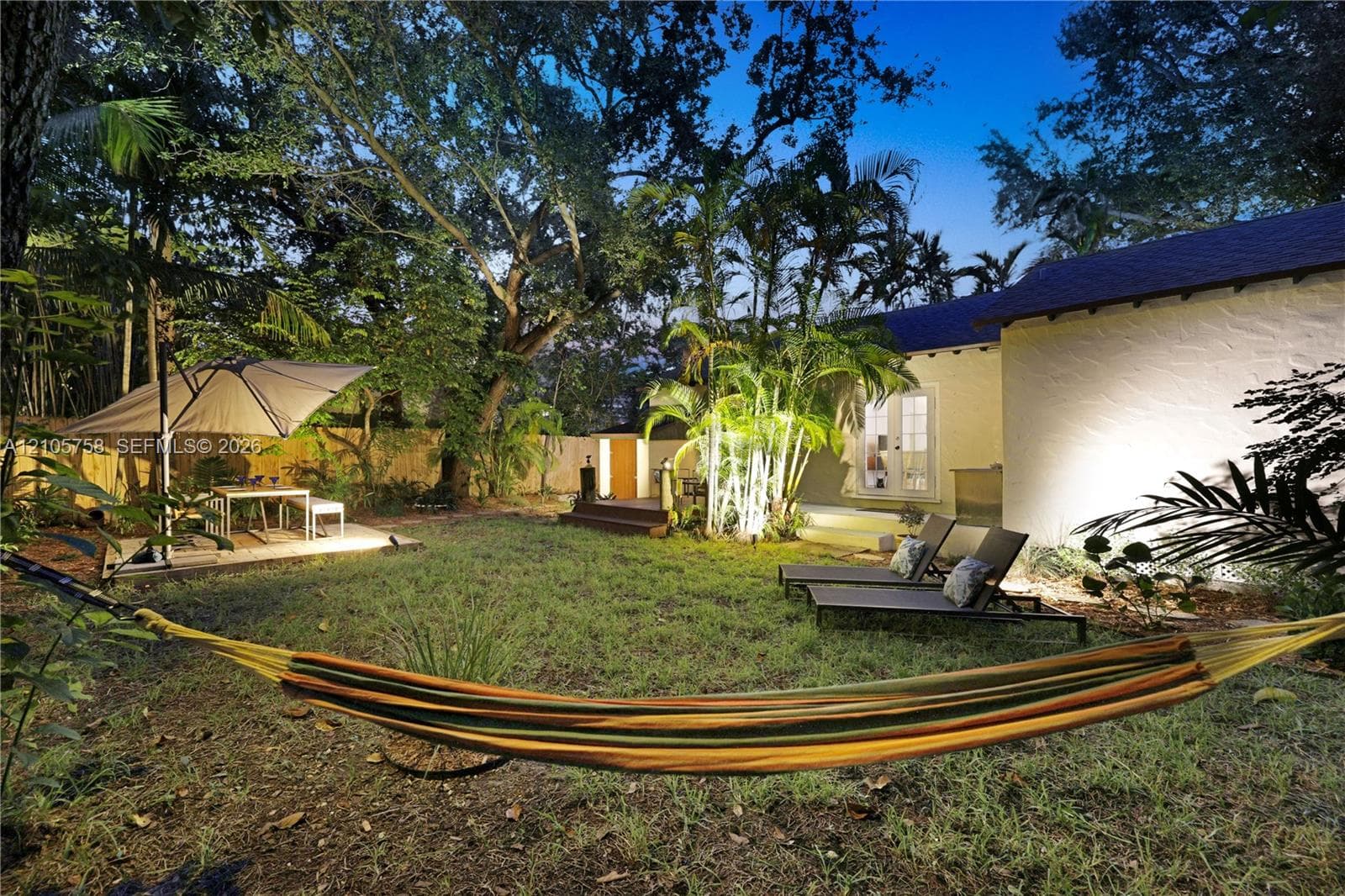 Private backyard featuring a manicured lawn, wood-finish decking, mature trees, and high-contrast exterior wall masonry