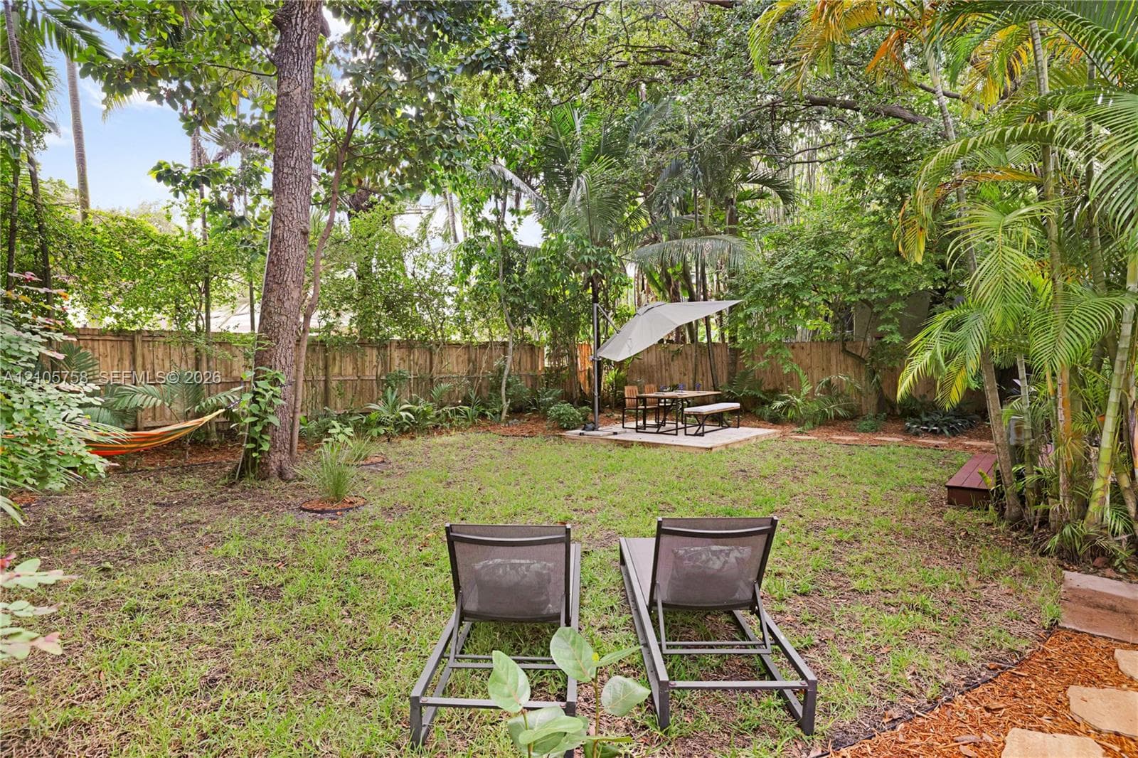 Expansive backyard featuring a lush landscape, mature trees, a natural-material privacy fence, and a paved patio area