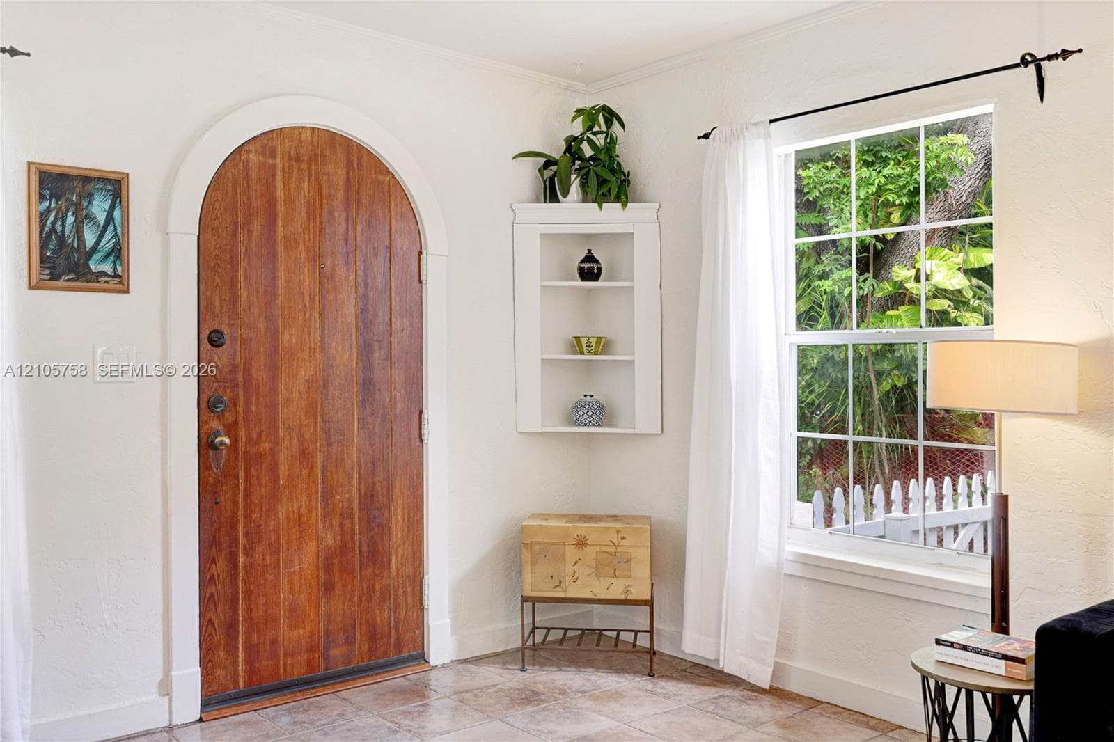 Arched wooden entrance door with metallic hardware, multi-pane window, and built-in corner shelving unit