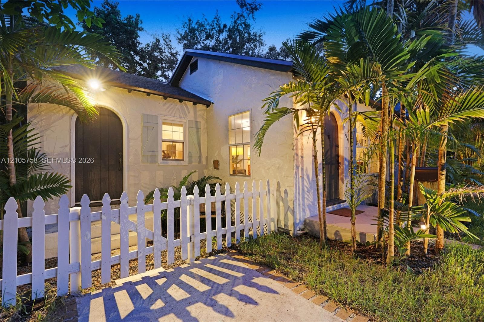 Stucco exterior featuring an arched entry, wood-finish shutters, a covered porch, and a picket fence