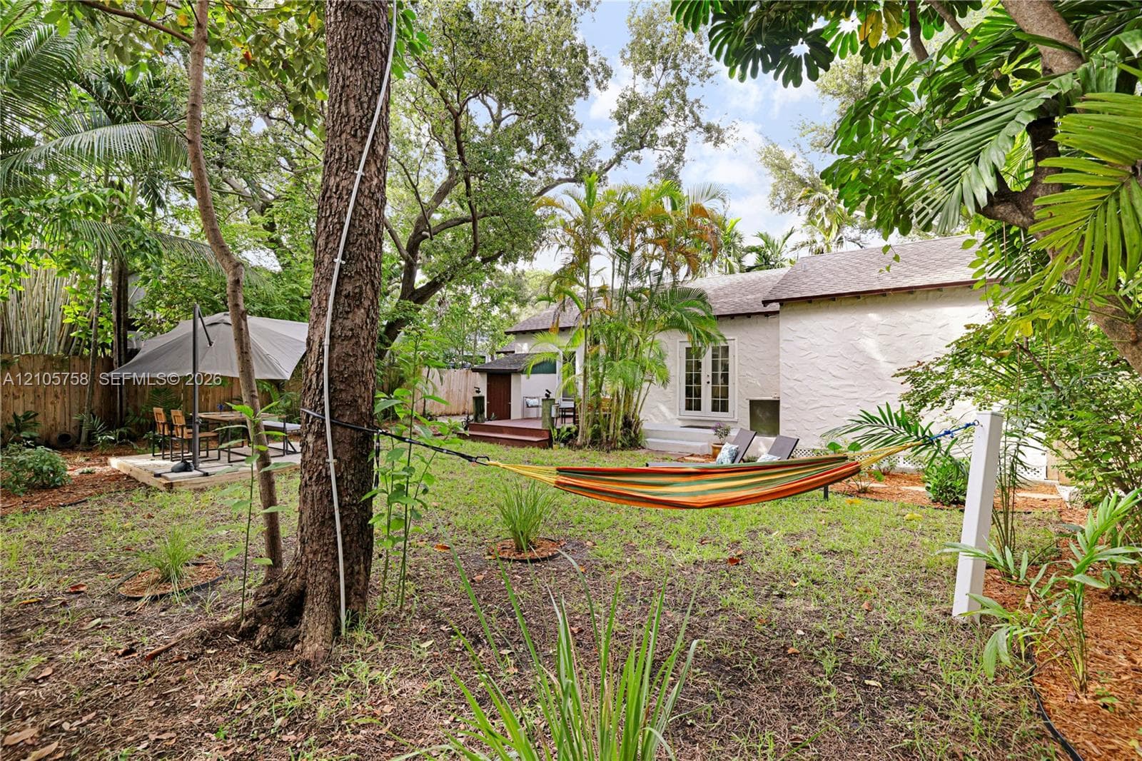 Expansive backyard featuring mature trees, wood decking, and white-stucco exterior finish