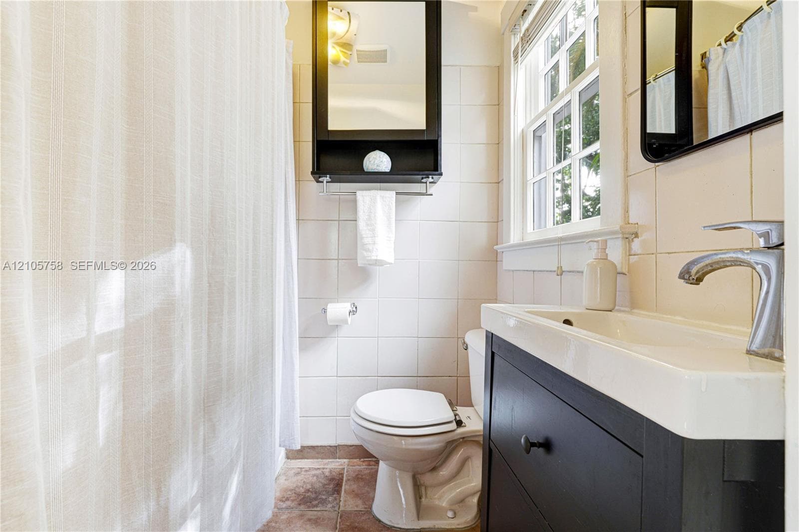 Bathroom featuring a dark wood-finish vanity with an integrated rectangular basin, a wall-mounted mirrored medicine cabinet, square wall tiling, and a window with divided lites