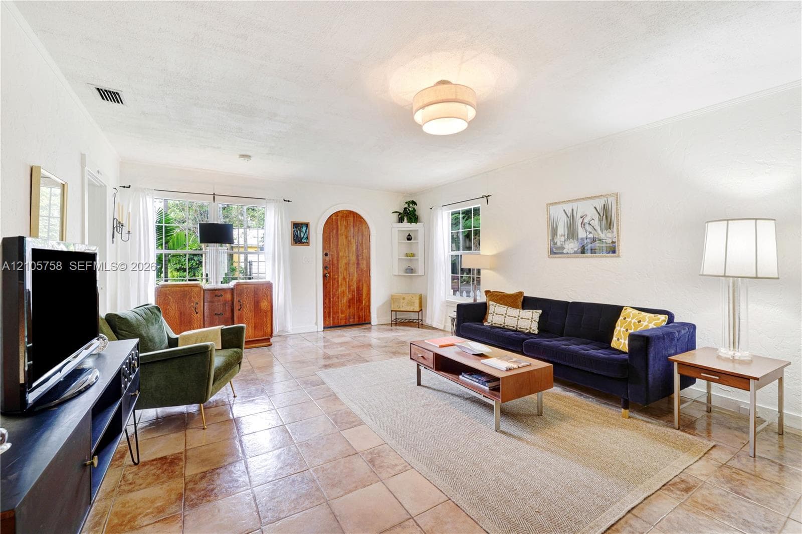 Spacious living area featuring square tile flooring, arched wooden entry door, multi-pane windows, and built-in corner shelving