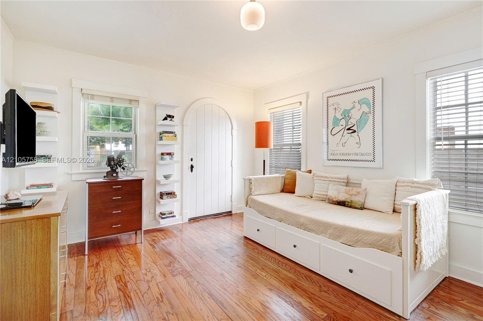 Arched solid-panel door featuring wood-finish flooring, built-in shelving units, and horizontal window blinds