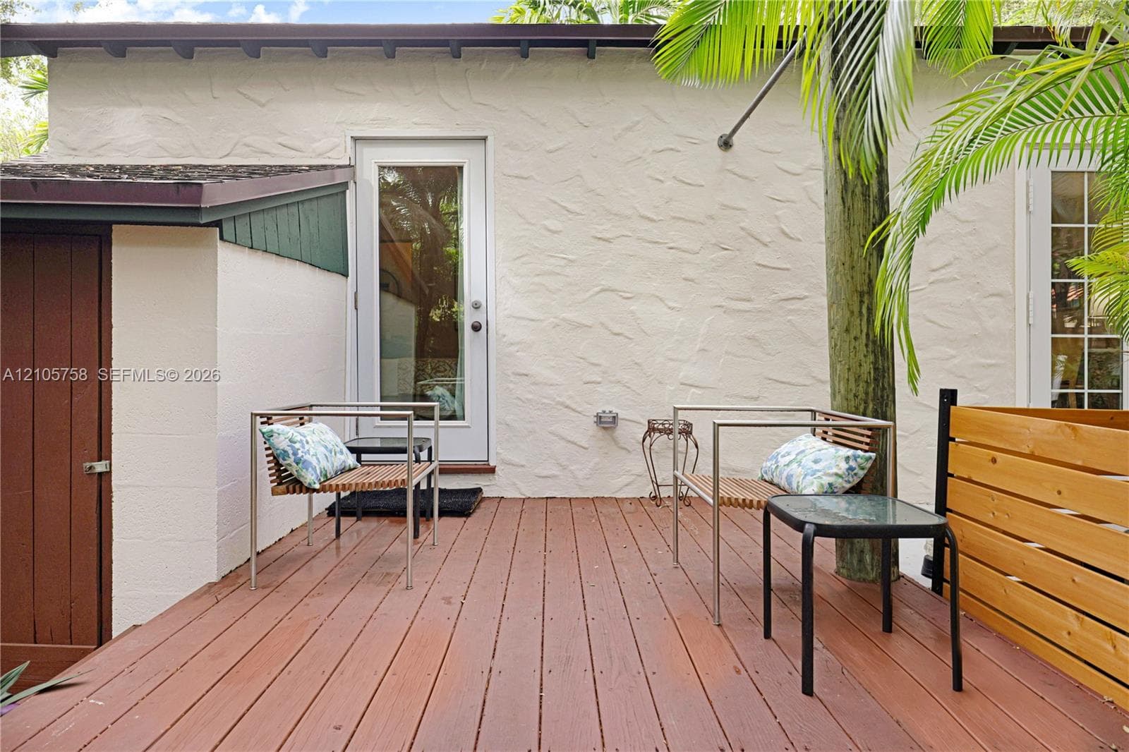 Textured stucco exterior featuring a wood-tone deck, horizontal wood-slat privacy fencing, and a paneled wood-finish access door