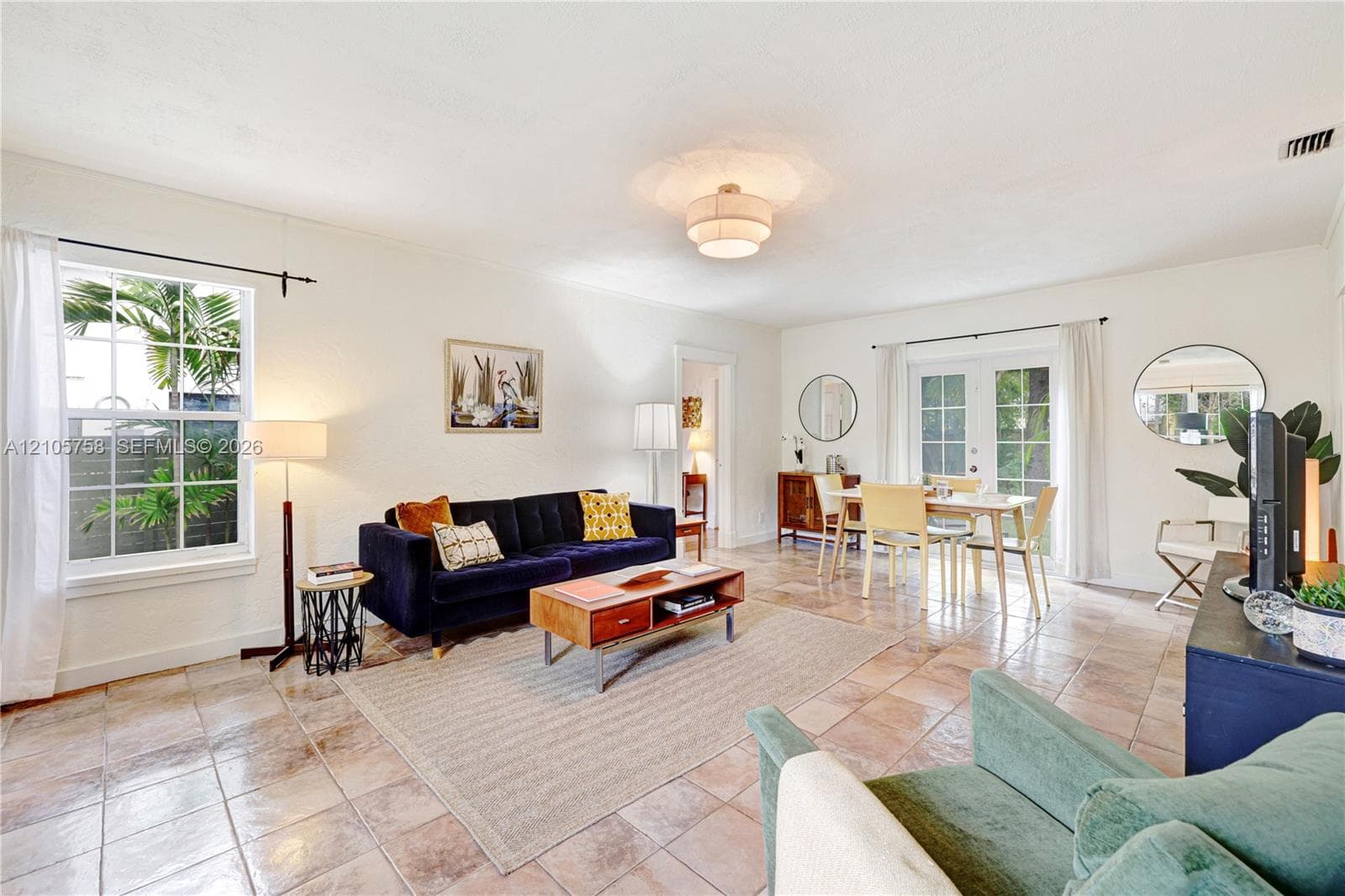 Open living area featuring large-format stone tile flooring, multi-pane windows, a central tiered flush-mount light fixture, and French doors