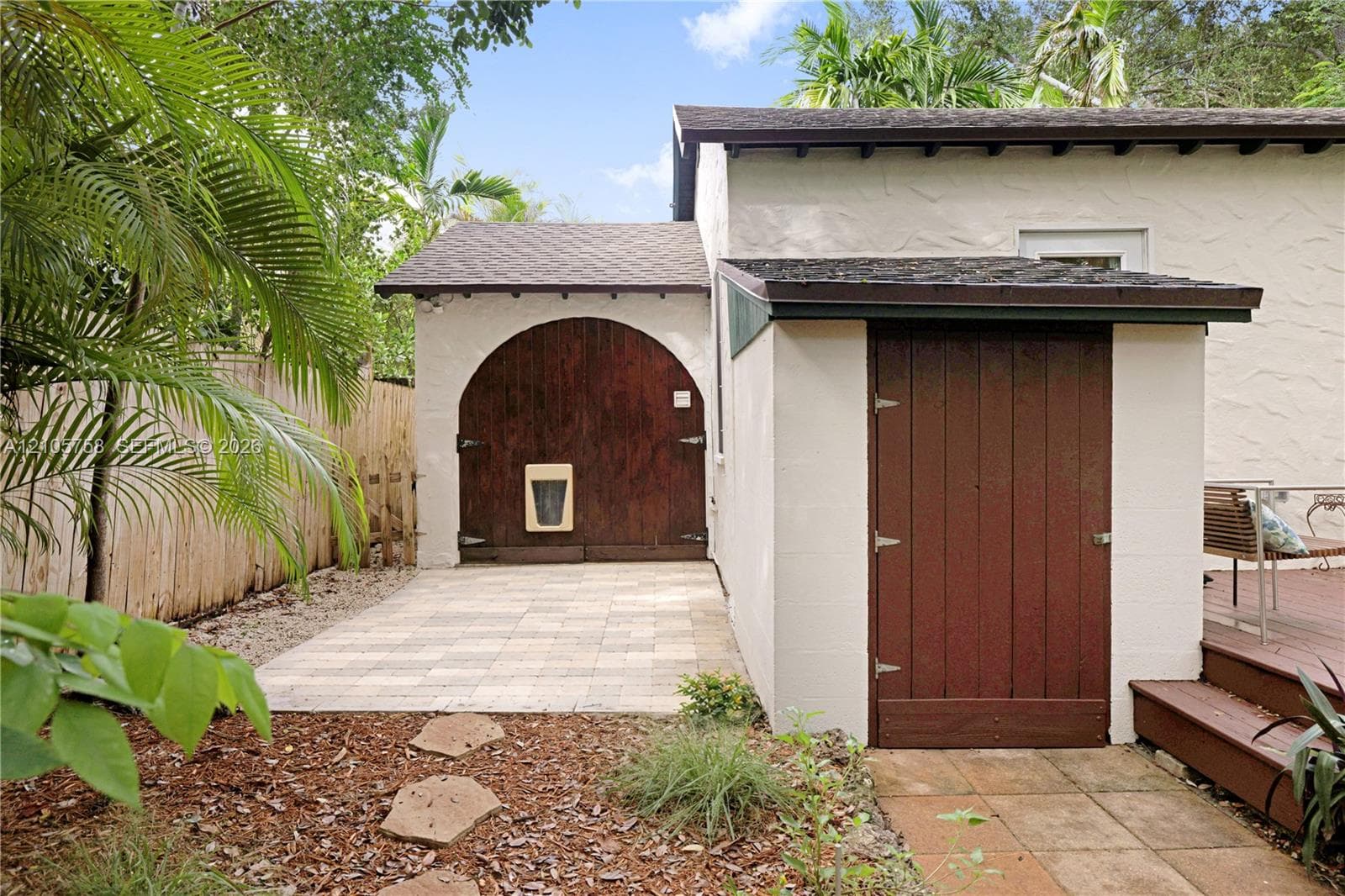 Stucco exterior featuring a distinctive arched wood door, a separate wood-panel utility entry, paved stone patio, and wood decking