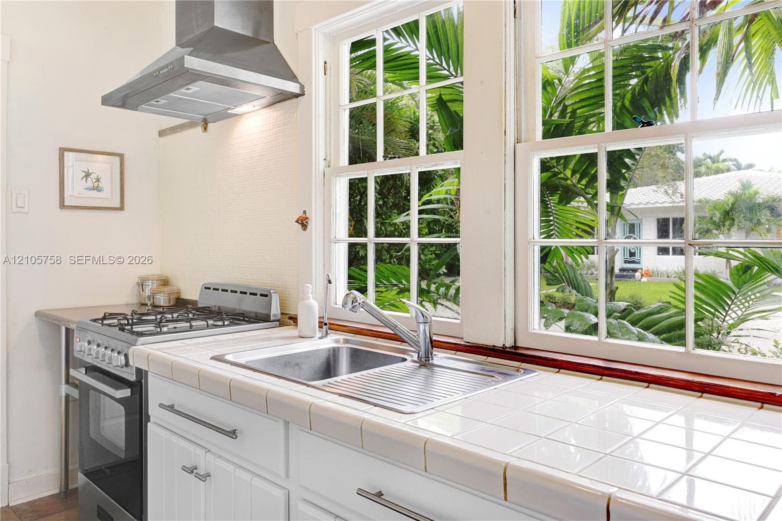 Kitchen featuring white tiled countertops, stainless steel dual-basin sink with a goose-neck faucet, freestanding stainless steel gas range, and a stainless steel vent hood