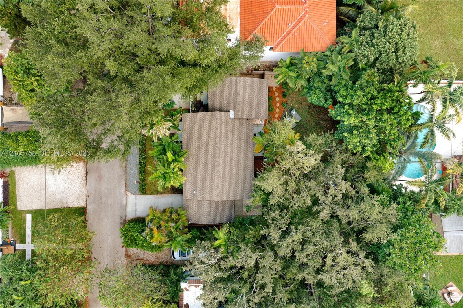 Aerial perspective of property featuring shingled roofing, paved driveway, mature canopy trees, and an in-ground swimming pool