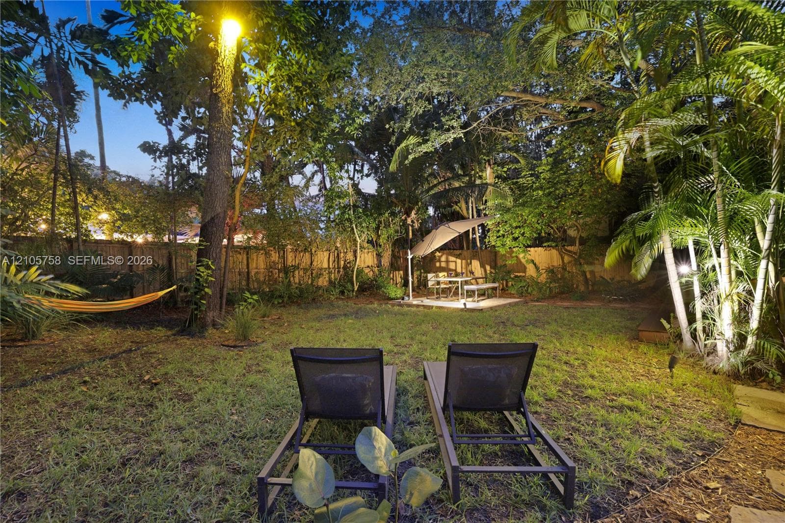 Private backyard featuring a fenced perimeter, mature trees, lush tropical landscaping, and a paved patio area