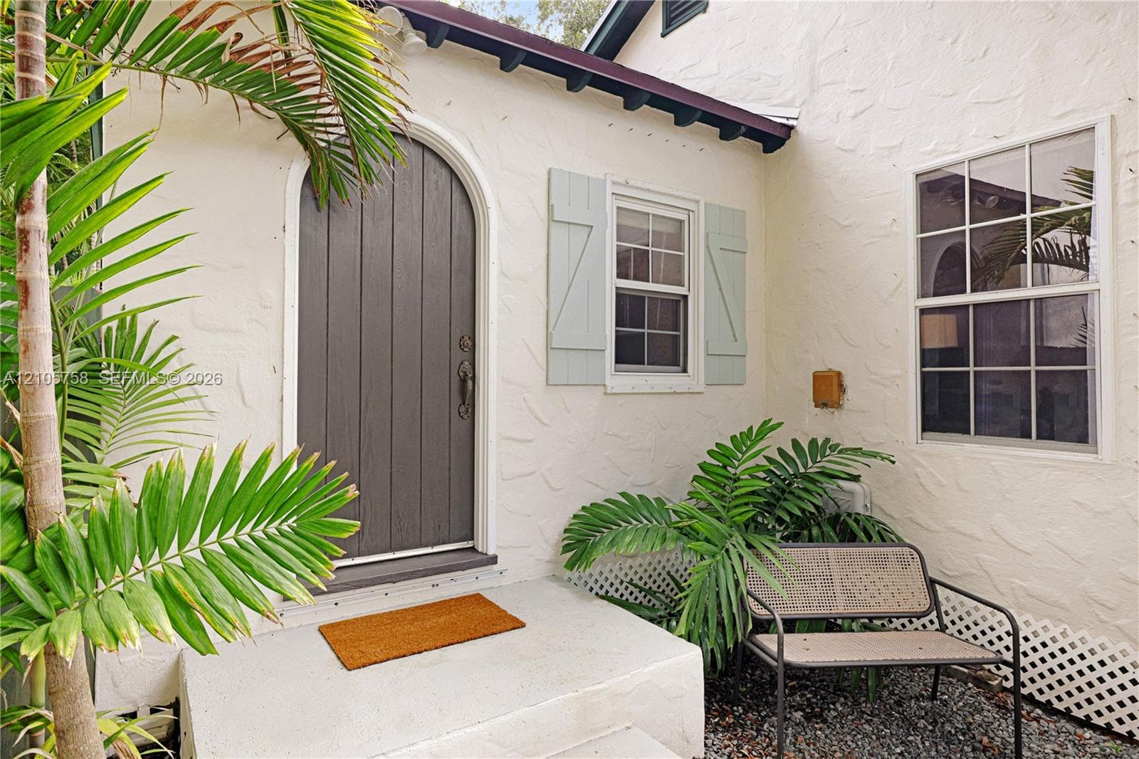 Textured stucco exterior featuring an arched entry door, paneled window shutters, and a concrete stoop