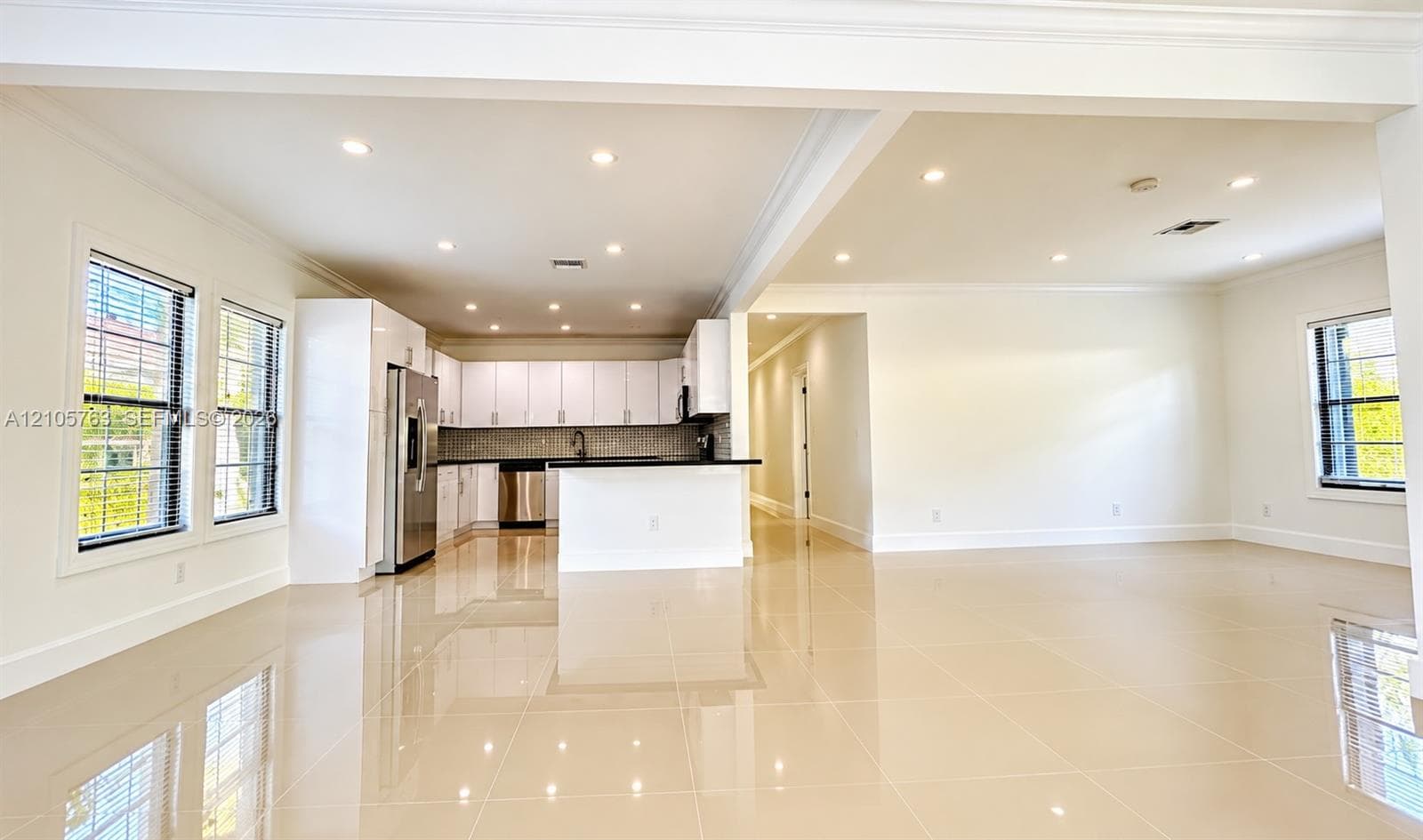 Open-concept area featuring polished tile flooring, recessed lighting, white cabinetry, a center island with a dark countertop, and stainless steel appliances